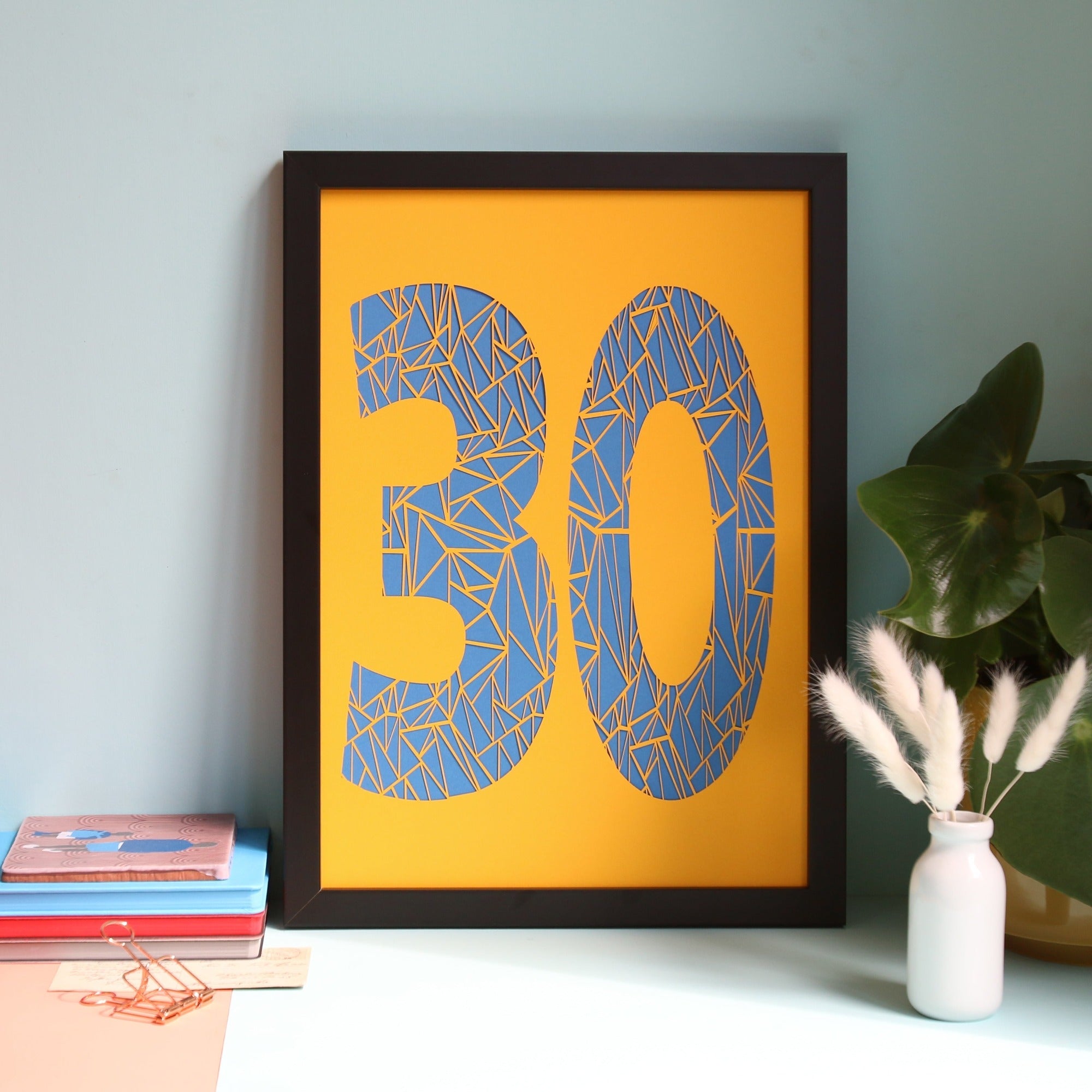 Yellow framed papercut with a geometric 30 highlighted in blue