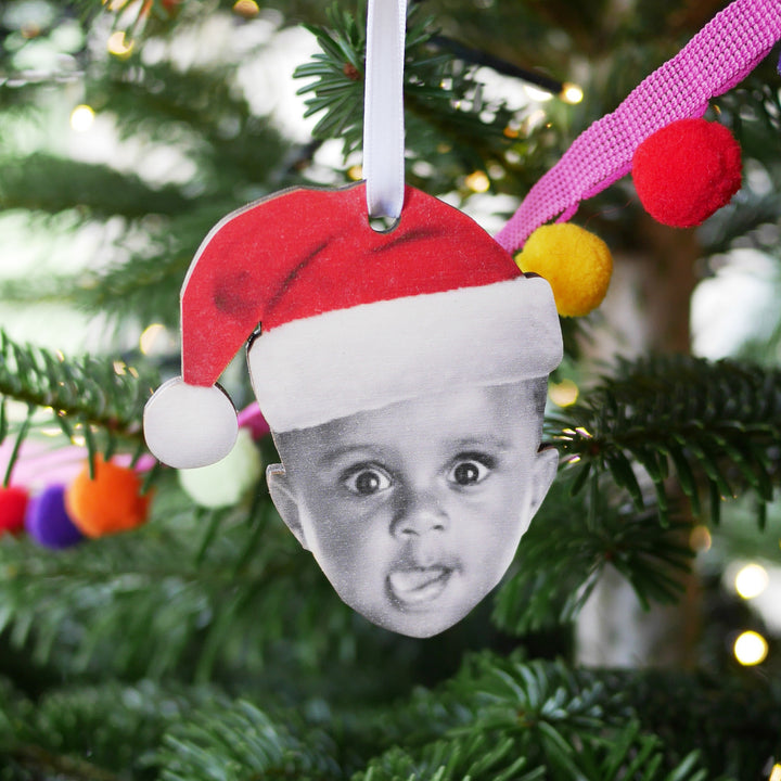 Personalised wooden Christmas bauble with toddler in Santa hat, hanging on festive tree.