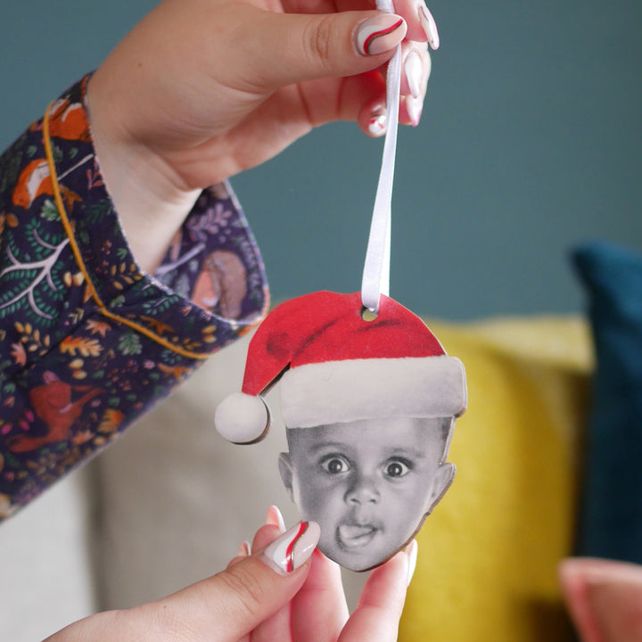 Personalised wooden Christmas bauble with a toddler wearing a Santa hat held in hand.