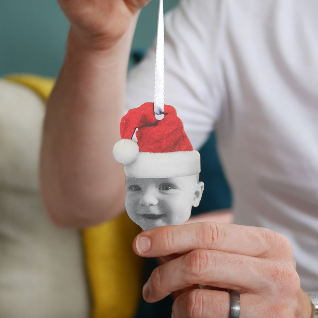 Personalised wooden Christmas bauble with baby wearing Santa hat held in hand.