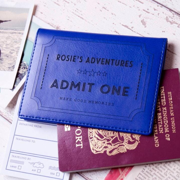 A blue travel wallet embossed with "Rosie's Adventures - Admit One - Make Good Memories" rests on passports, tickets, and travel documents.