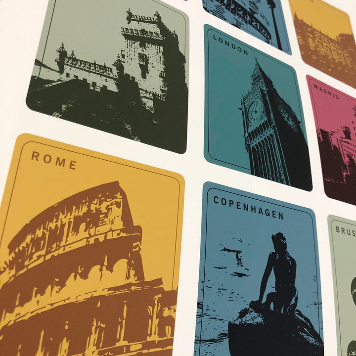 Close-up of a framed print with nine city landmark squares, featuring the Colosseum in Rome, Big Ben in London, and the Little Mermaid in Copenhagen. Each square has a city name and silhouette of its landmark.