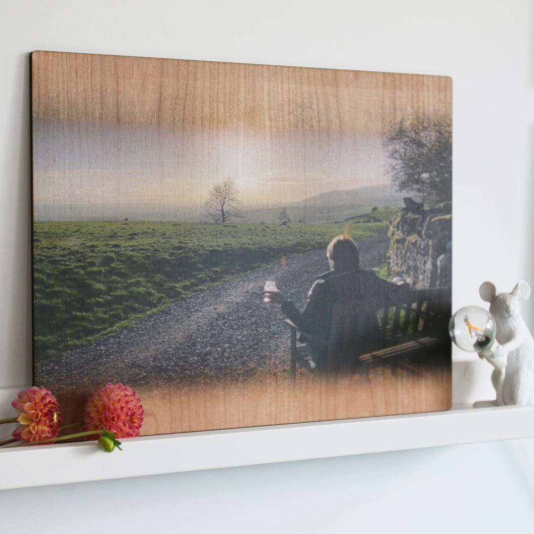 A photo of a person sitting on a bench, enjoying a drink with a beautiful sunset view, printed on a wooden plaque.
