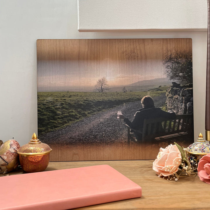 A photo of a person sitting on a bench, enjoying a drink with a beautiful sunset view, printed on a wooden plaque.
